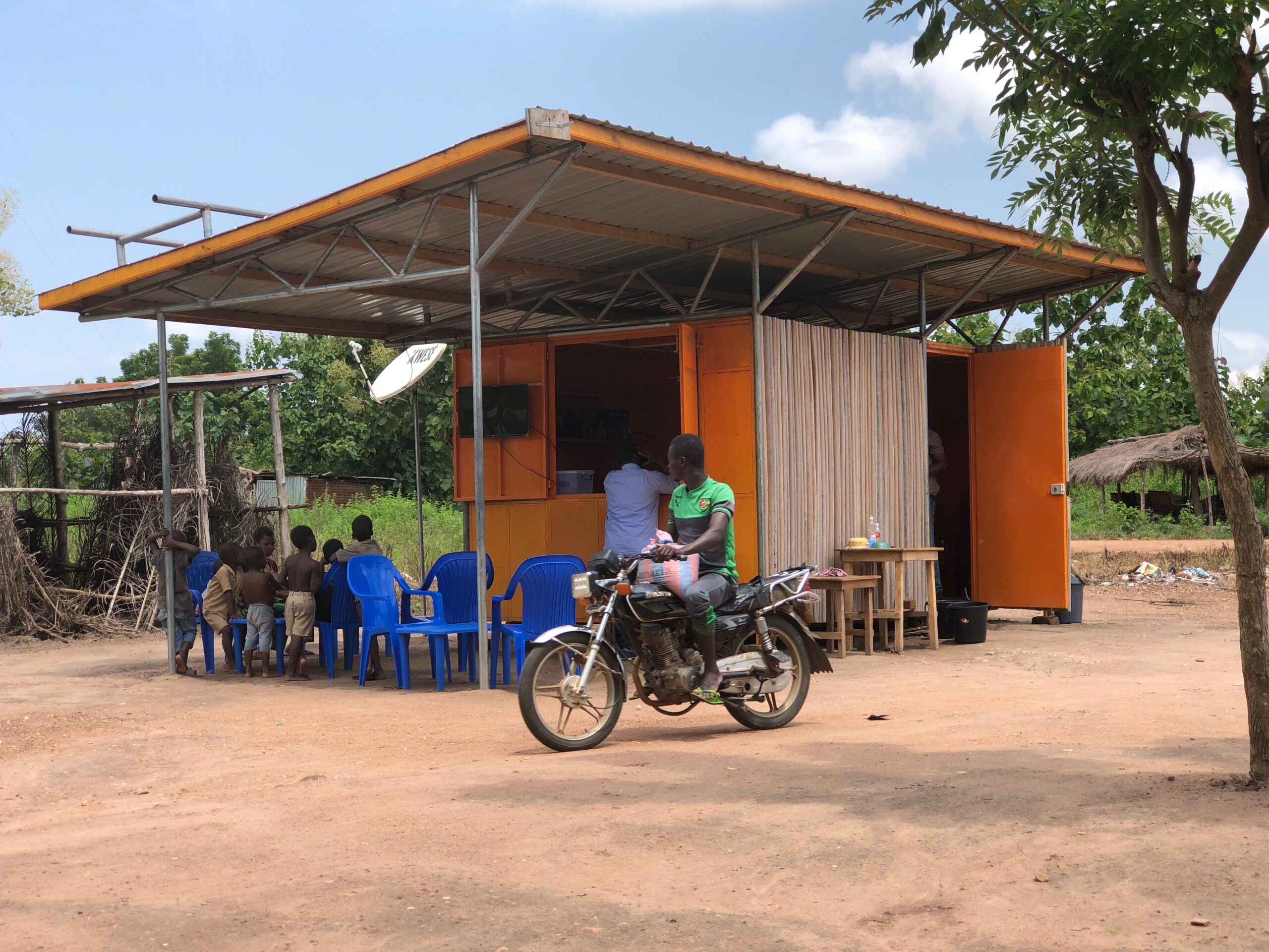 Une moto passe devant un kiosque solaire Benoo Energies dans un village au Togo en Afrique